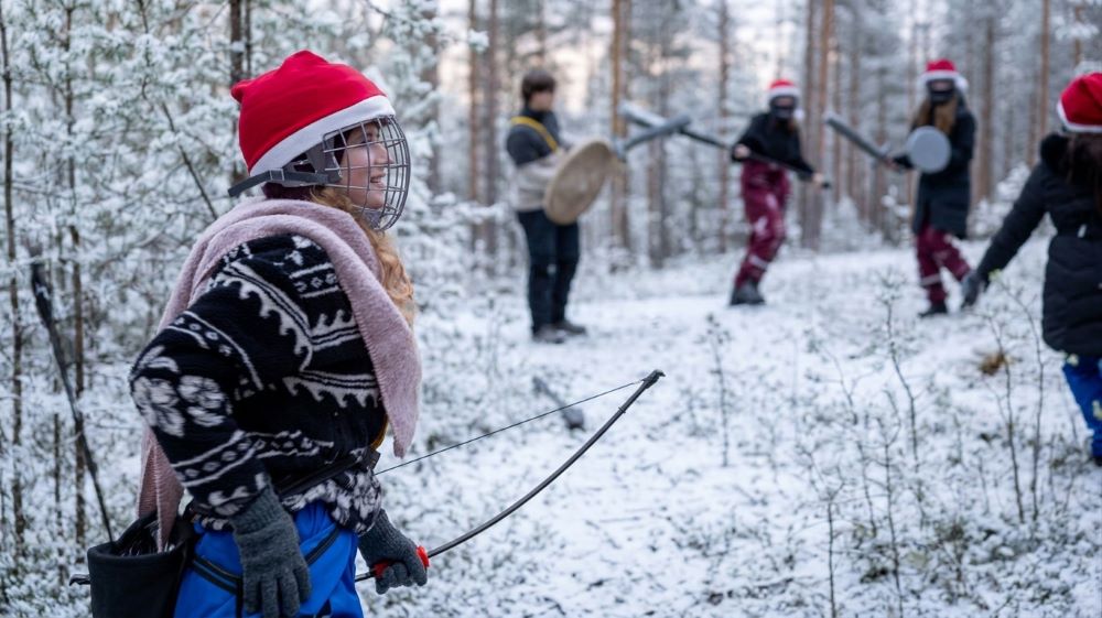 A smiling recruit holds a bow while others spar in the background