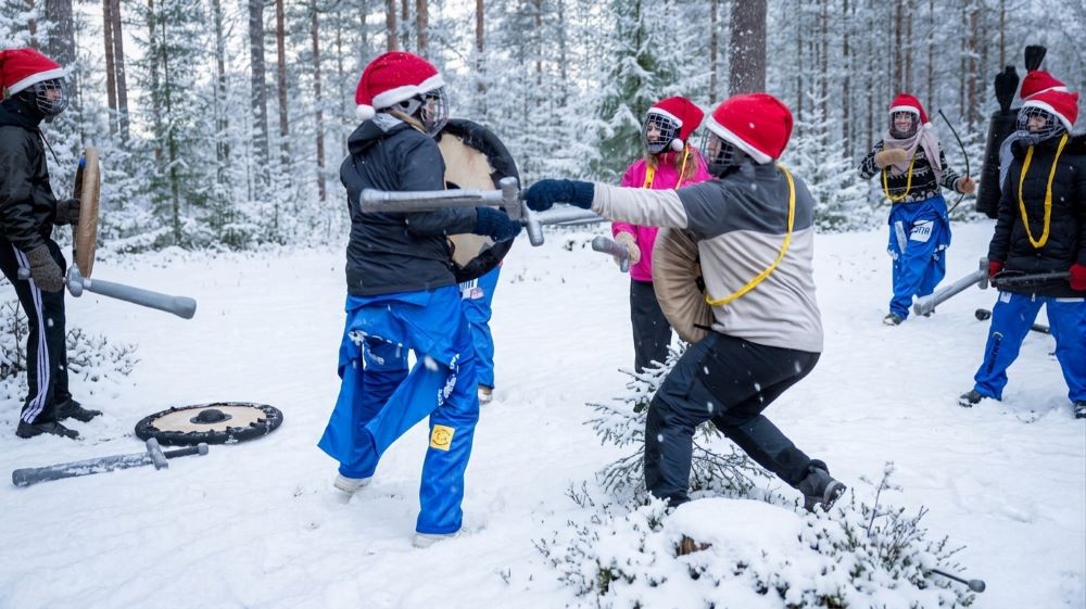 Recruits in Santa hats and helmets duel with padded swords and shields in a snowy forest
